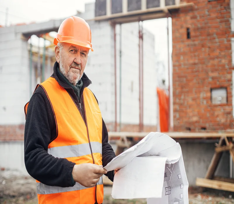 Experienced masonry contractor in safety gear reviewing blueprints at a brick construction site